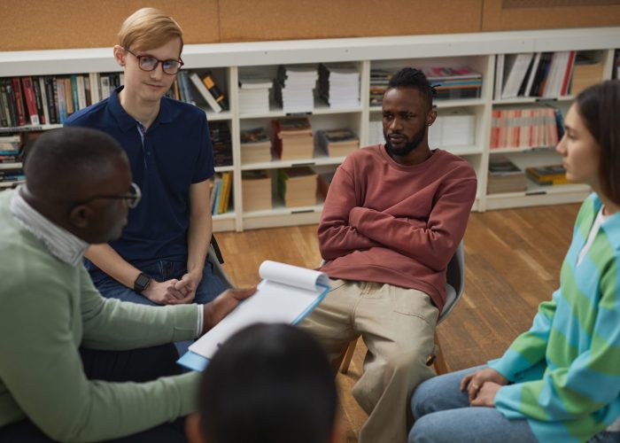High angle view at diverse group of young people sitting in circle during therapy session in college with male psychologist
